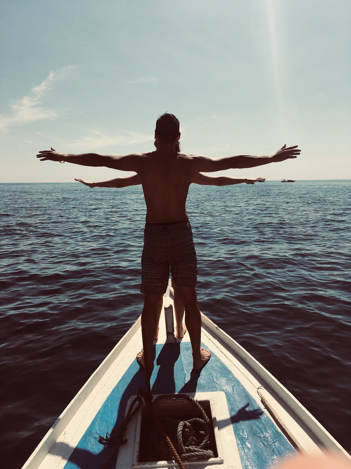 Person standing at the bow of a boat with outstretched arms.