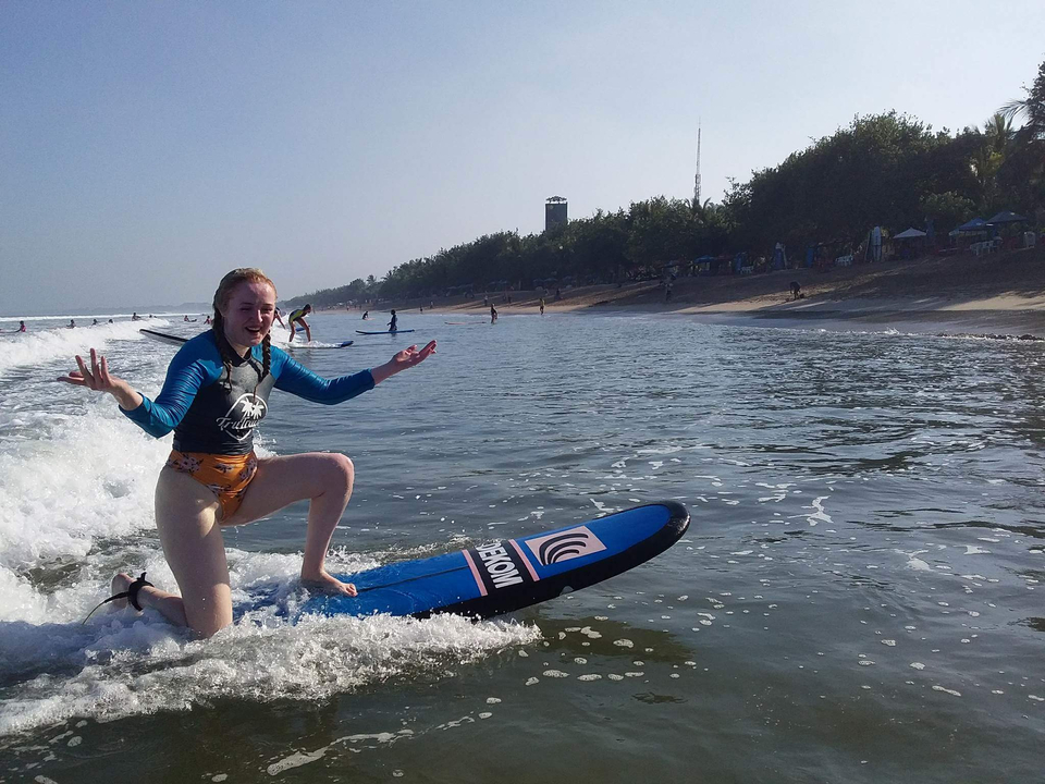 Person surfing on a board in the ocean while smiling at the camera.