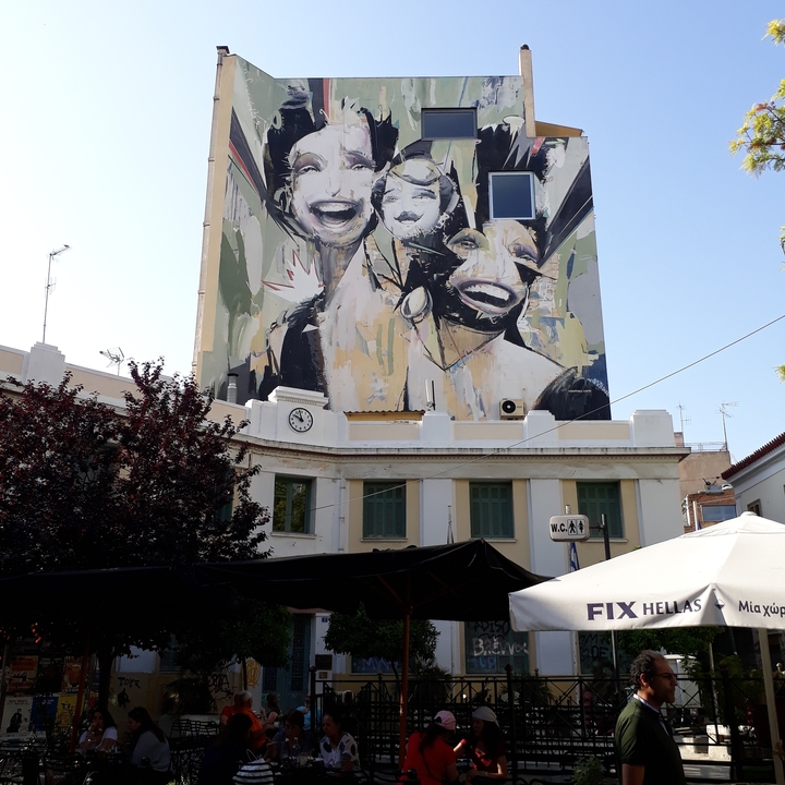 Façade d'un bâtiment ornée d'une peinture murale colorée représentant de grands visages souriants.