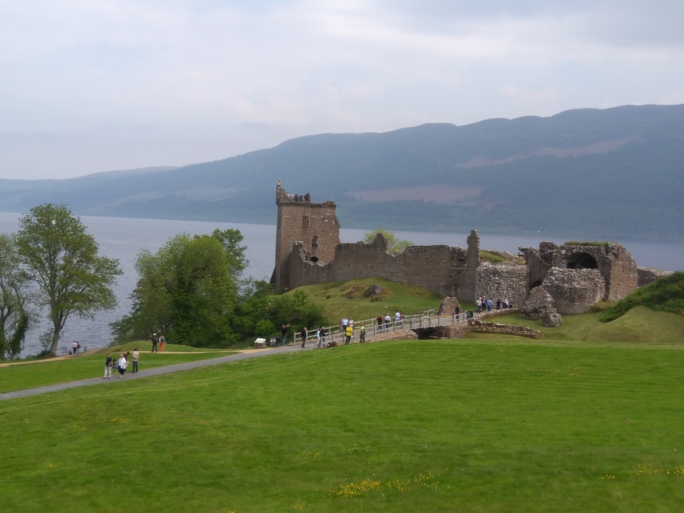 Ruines d'un château au bord d'un loch avec des visiteurs qui se promènent.