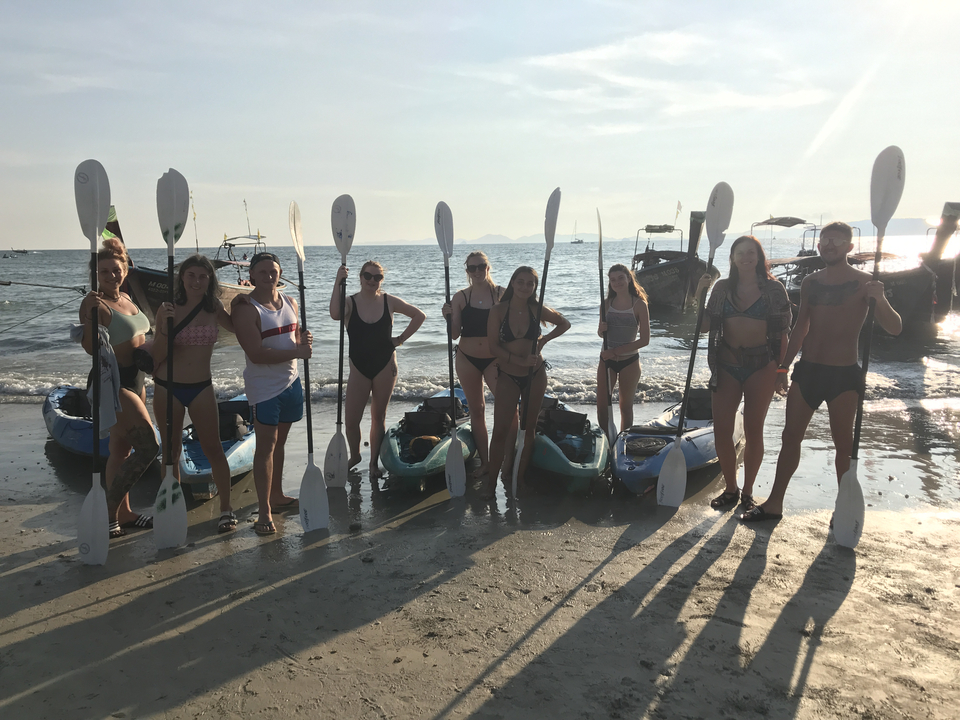 Group standing with paddles and kayaks on a beach.