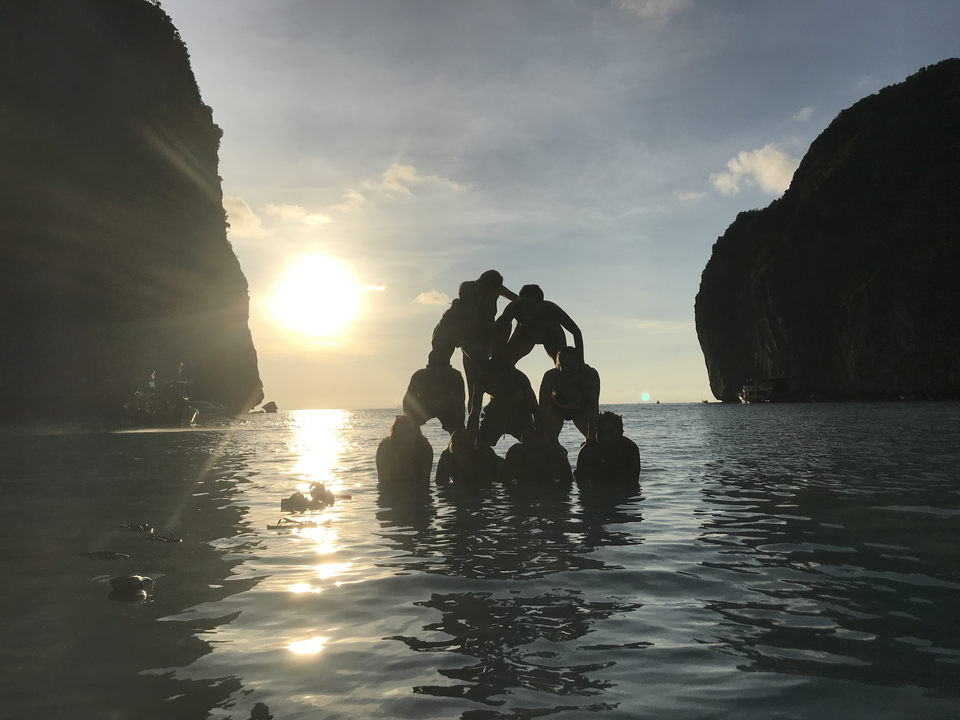 Silhouette of people forming a pyramid in water during sunset.
