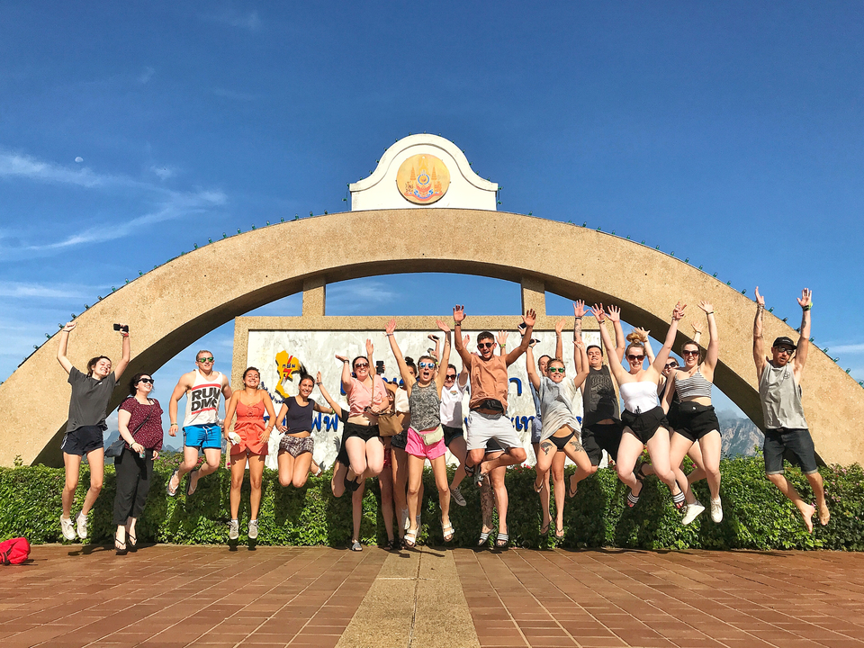 Group of people jumping in front of a sign with a clear blue sky.