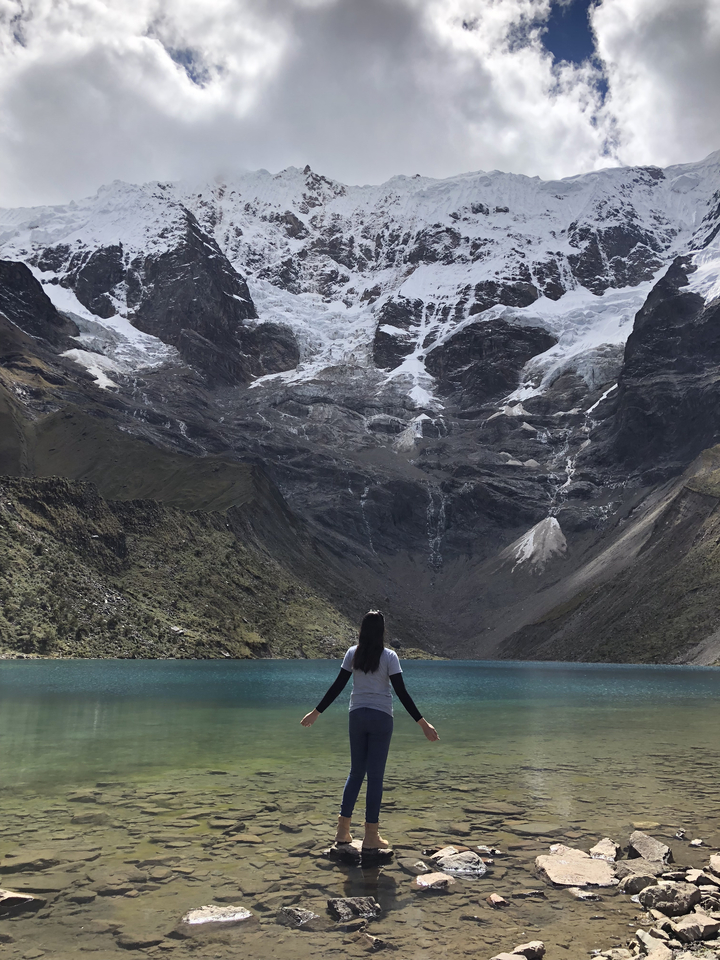 Personne se tenant au bord d'un lac de montagne avec des sommets enneigés.