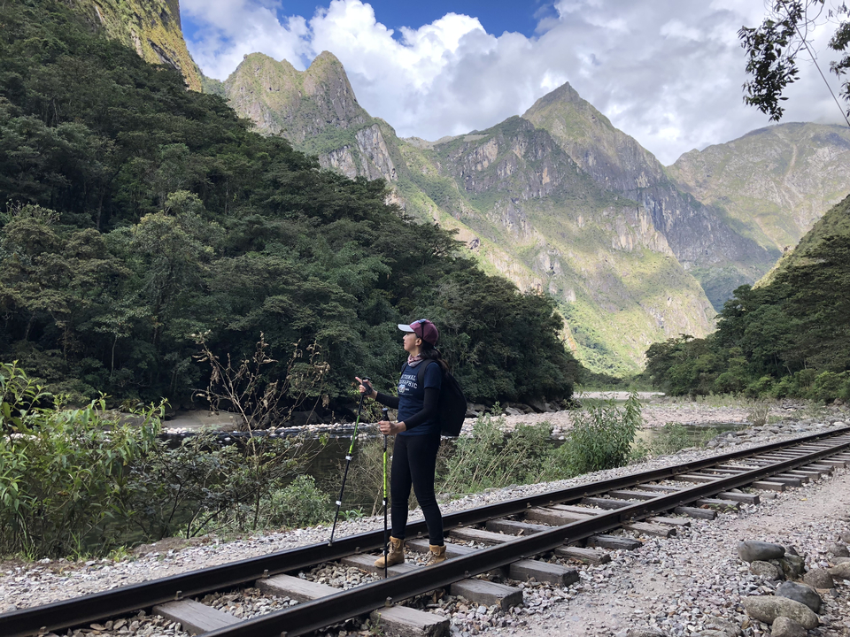 Une personne fait une randonnée le long de la voie ferrée avec des montagnes en arrière-plan.
