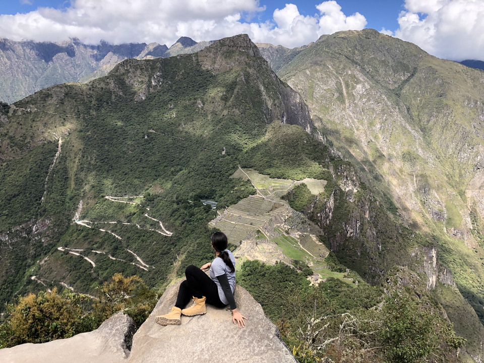 Personne assise sur un rocher surplombant de loin le Machu Picchu.