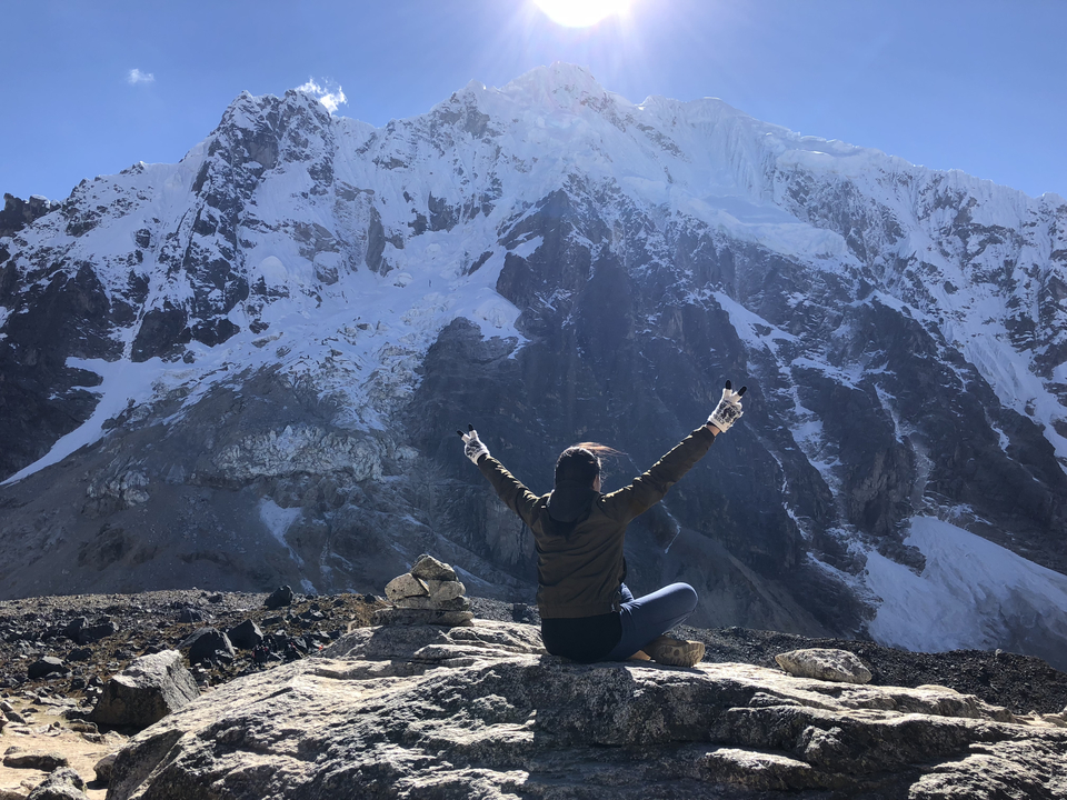 Personne assise, les bras levés, devant une montagne enneigée.
