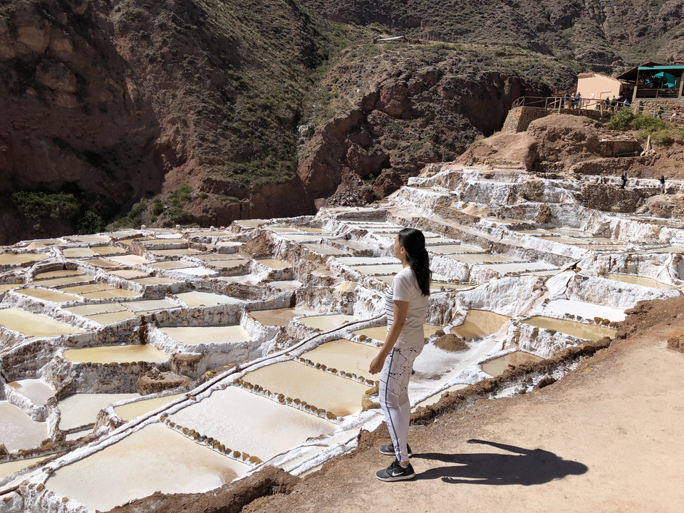 Une personne face aux terrasses de sel de Maras, avec en toile de fond des collines rocheuses.