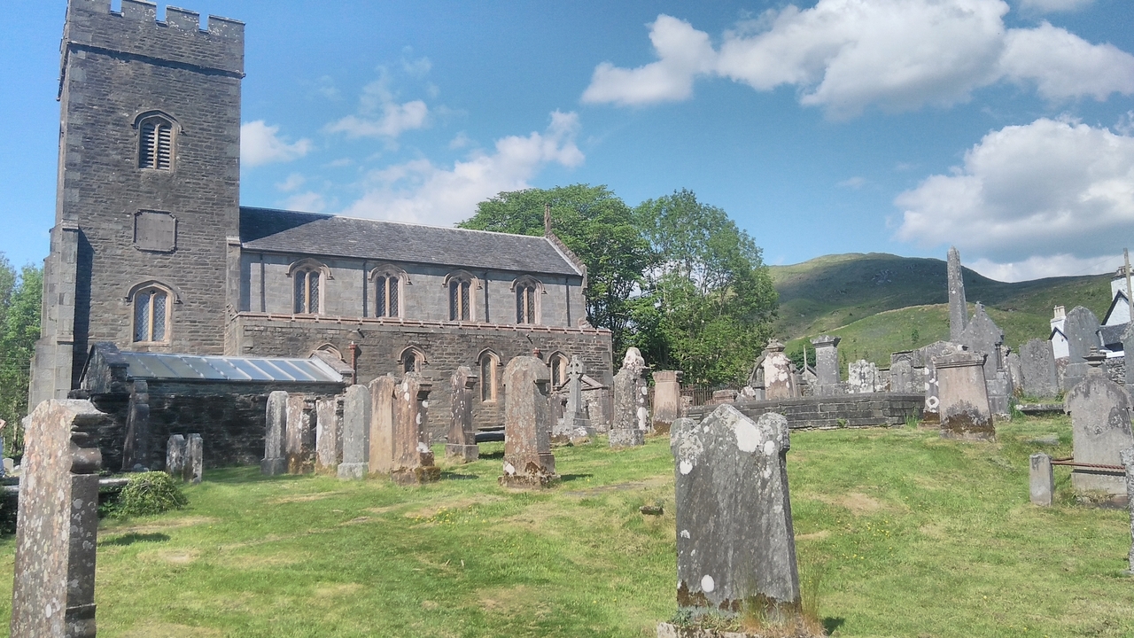 Vieille église entourée d'un cimetière avec des montagnes en arrière-plan.