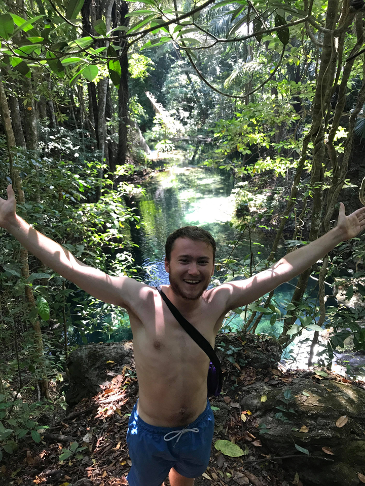 Man posing in front of a clear stream in a forest.