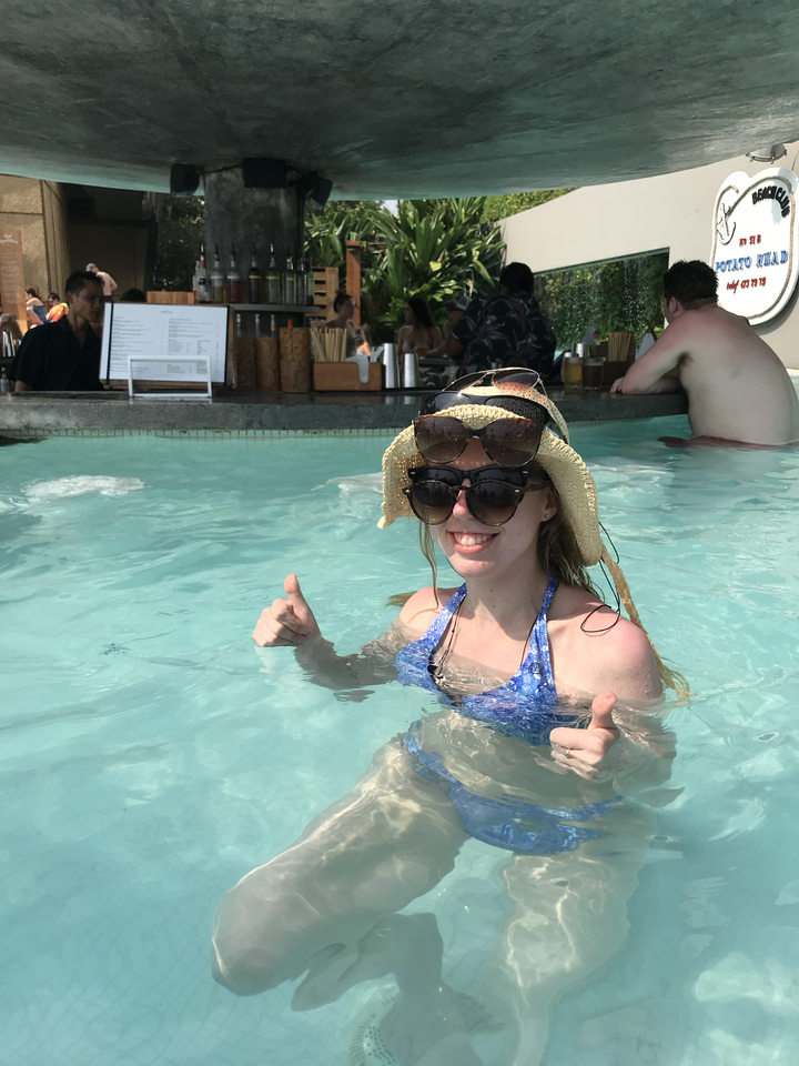 Person in a pool with sunglasses stacked on their hat.