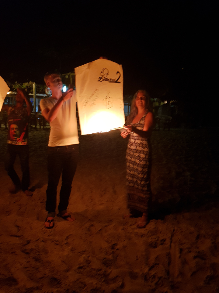 Des personnes lancent une lanterne sur une plage la nuit.