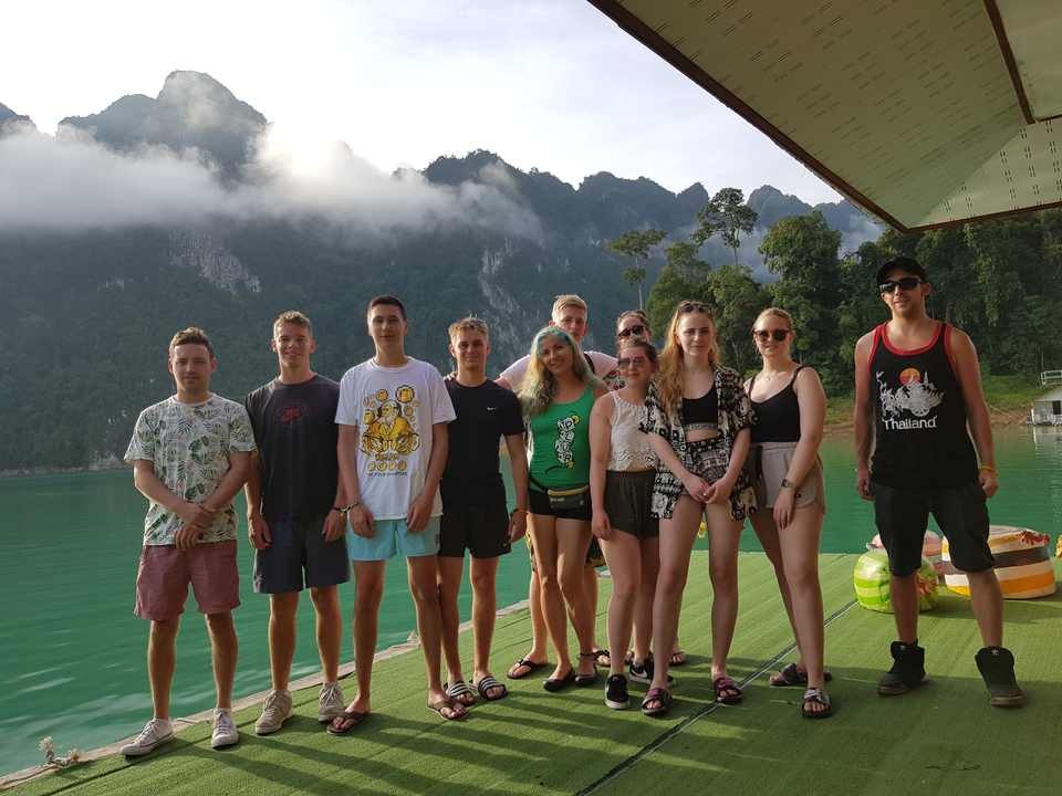 Un groupe d'amis posant sur une maison flottante avec une vue panoramique sur les montagnes.