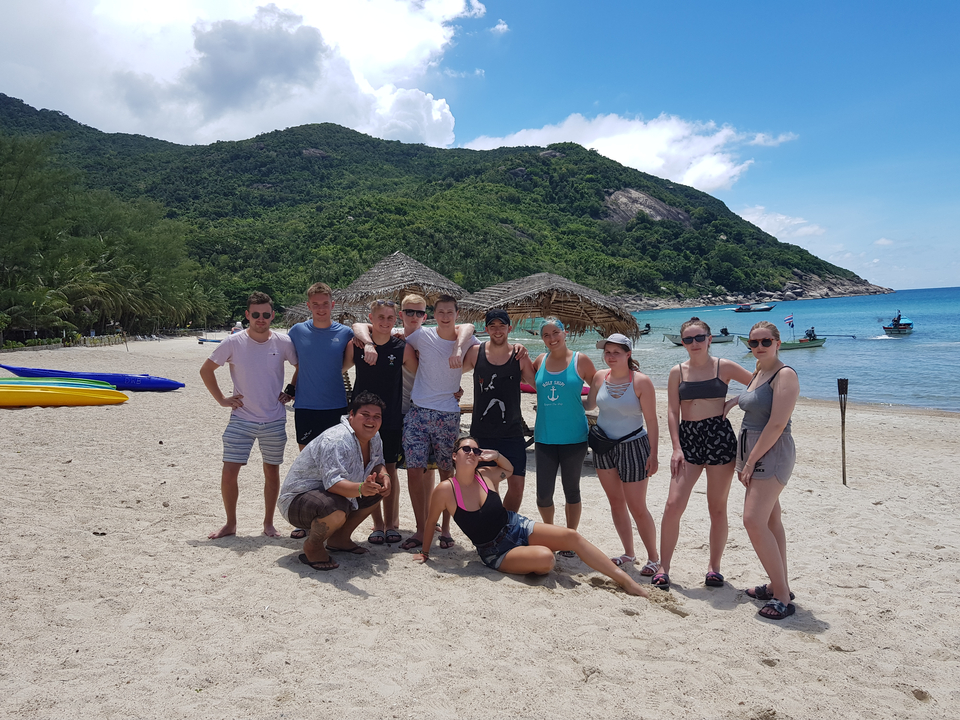 Un groupe d'amis posant sur une plage avec des palmiers et une montagne en arrière-plan.