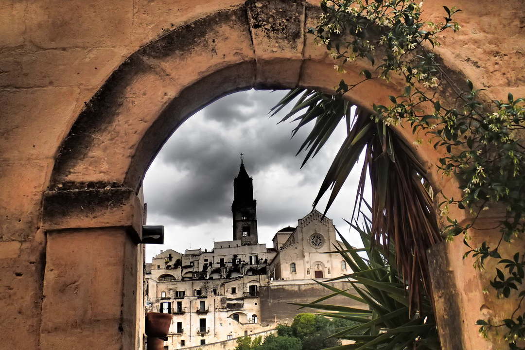 Vue de Matera encadrée par une ancienne arche avec des nuages au-dessus de la tête.