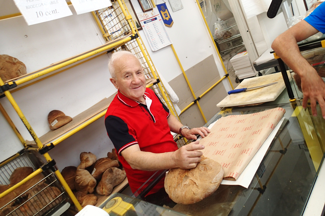 Homme âgé dans une boulangerie, en train d'emballer du pain.