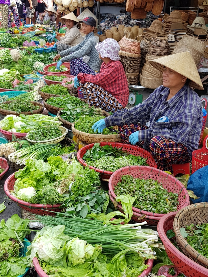 Scène de marché avec des paniers de légumes verts et des vendeurs.