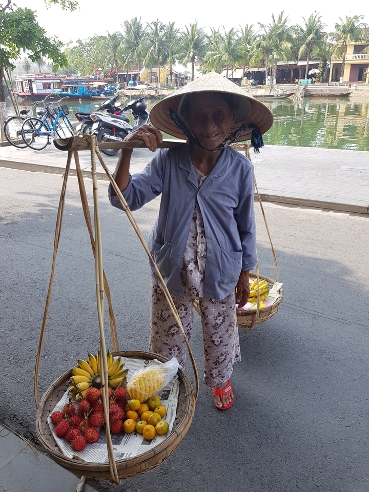 Femme portant des paniers traditionnels sur une route.