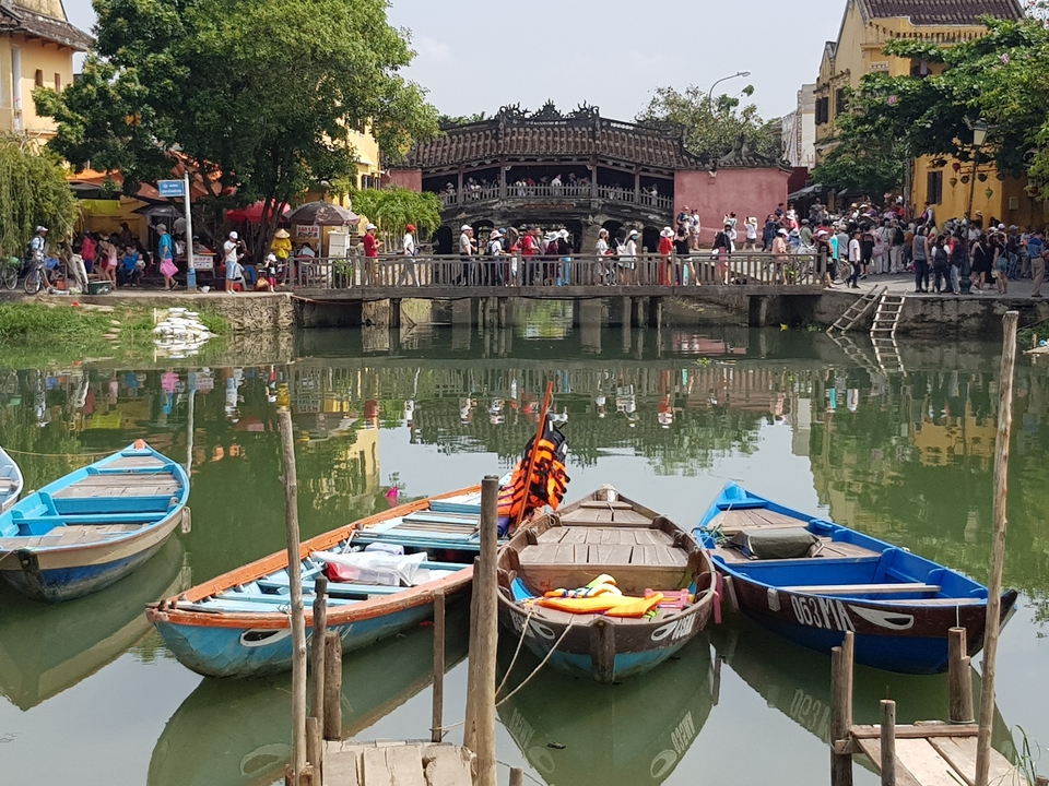 Bateaux colorés amarrés sur une rivière avec un pont en arrière-plan.
