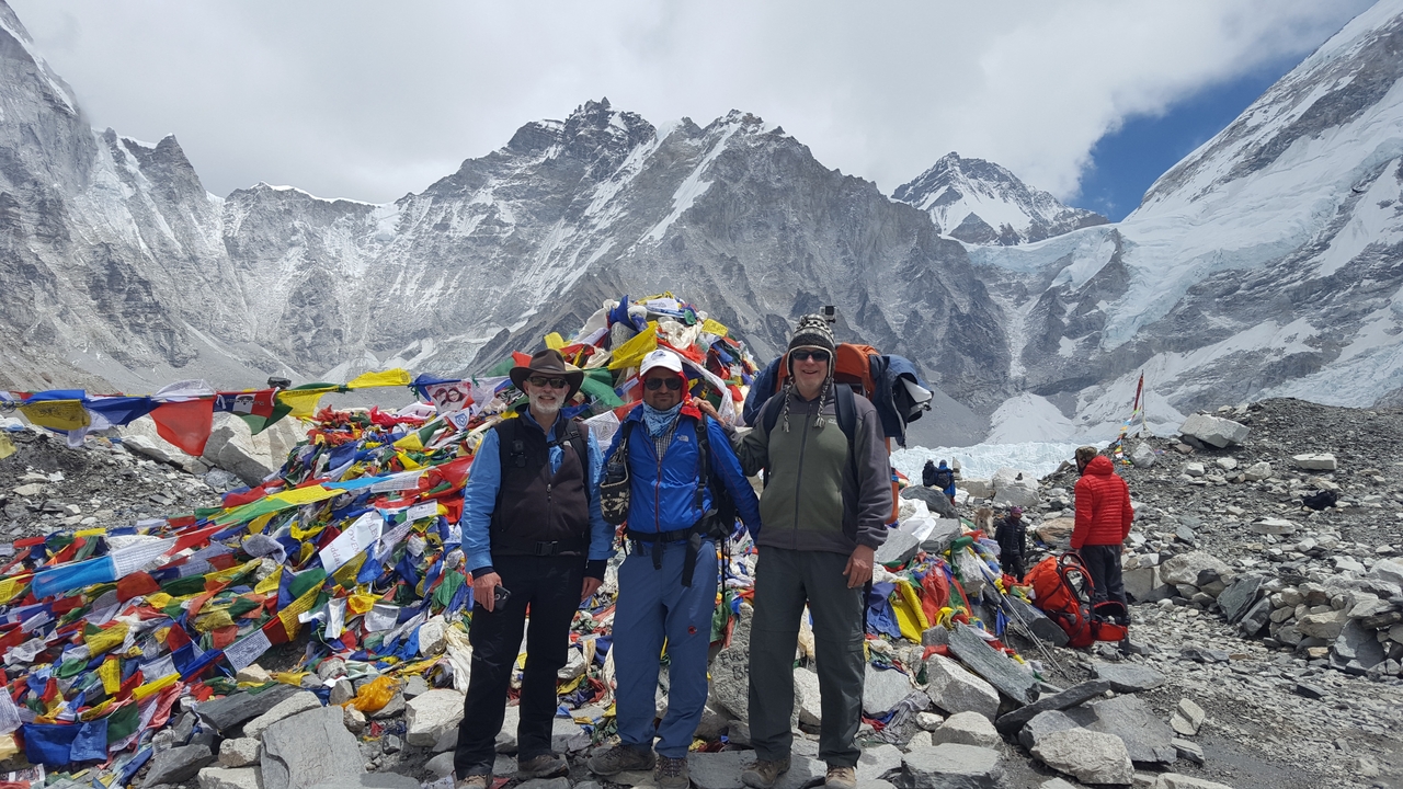 Trois personnes debout près de drapeaux de prière et d'un terrain montagneux.