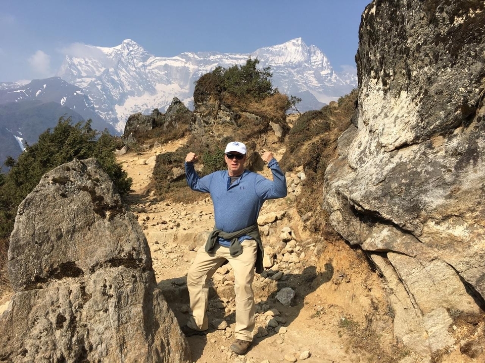 Personne posant de manière ludique sur un sentier de montagne avec des rochers et des sommets lointains.