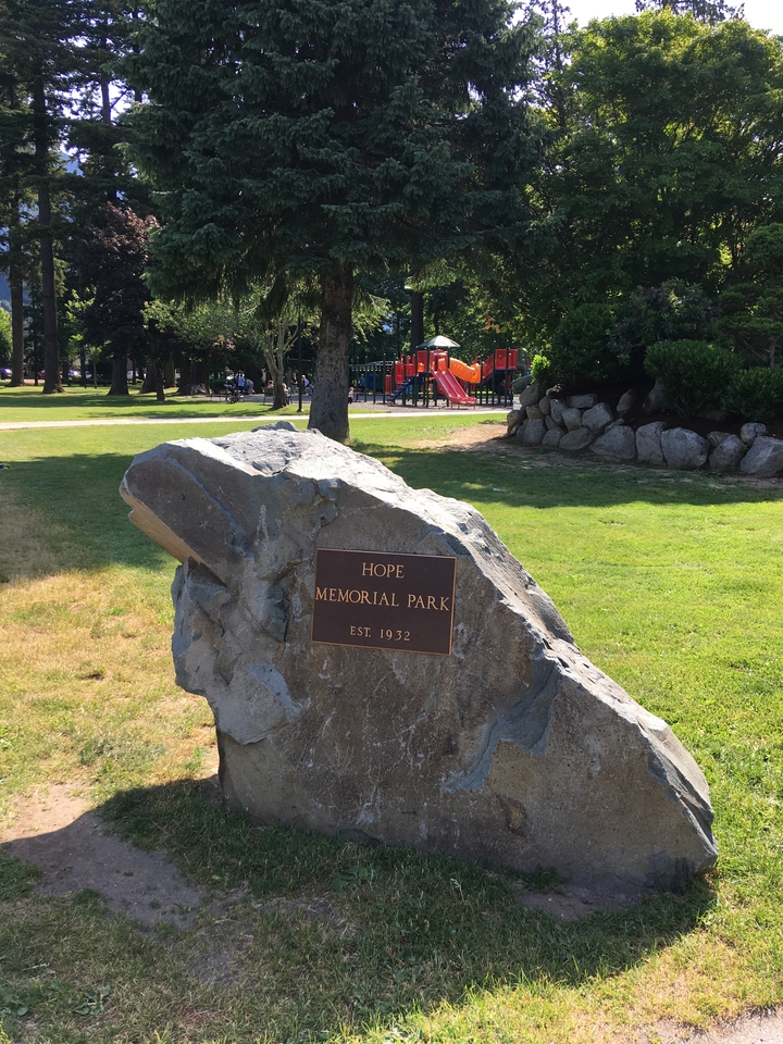 Un parc avec une pierre commémorative et une aire de jeux pour enfants à l'arrière-plan.