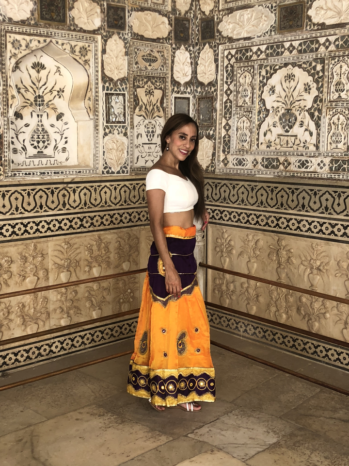 Femme posant à l'intérieur contre des murs décorés de façon complexe.