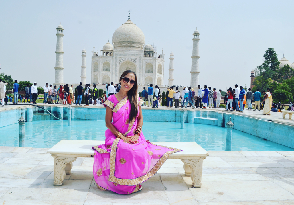 Femme assise devant le Taj Mahal, portant un sari traditionnel, avec une foule en arrière-plan.