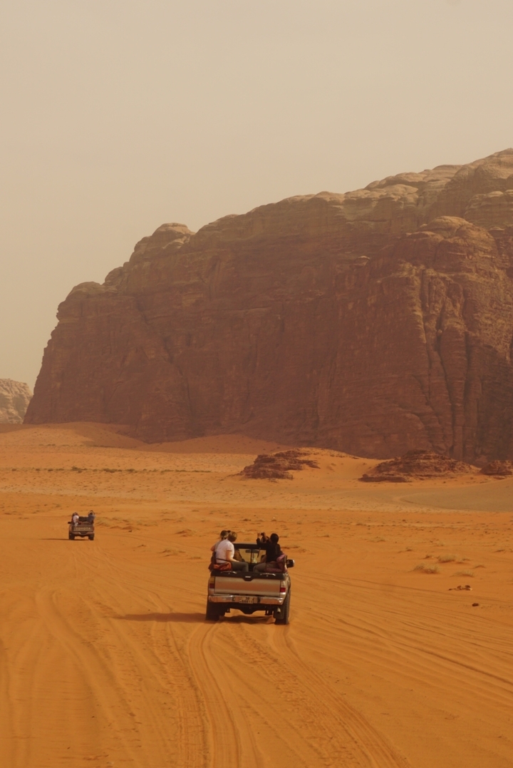 Grande falaise de grès dans le désert avec deux personnes à dos de chameau.