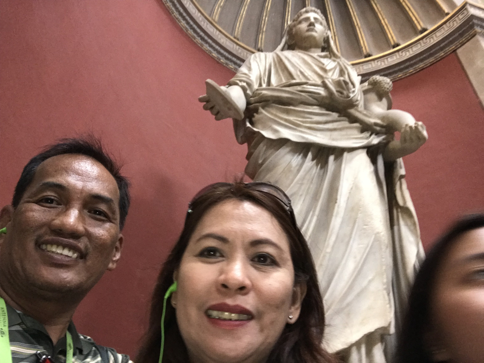 Two individuals posing in front of a statue.