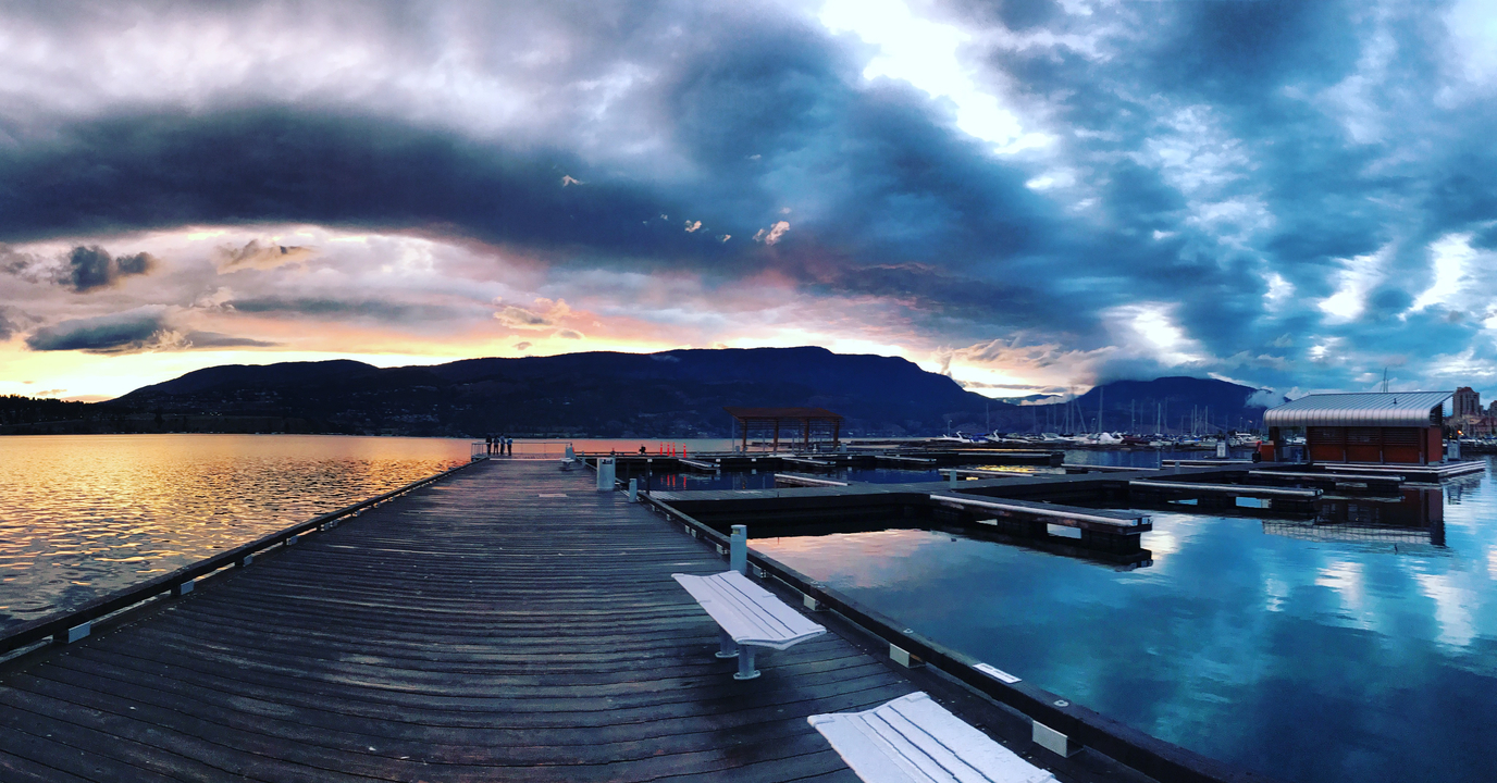 Dock, das in einen See mit dramatisch bewölktem Himmel bei Sonnenuntergang führt.