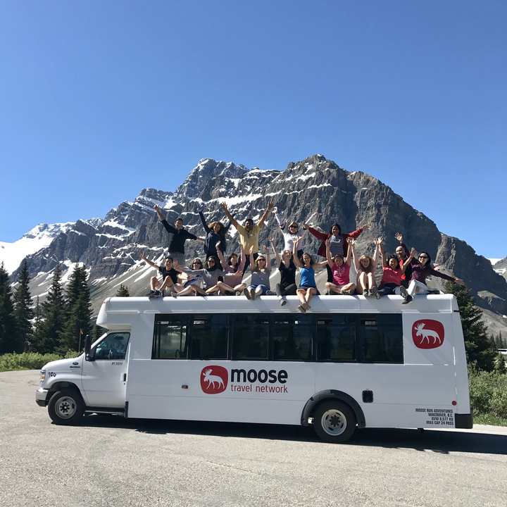 Eine Gruppe von Menschen sitzt auf einem Reisebus mit Bergkulisse.