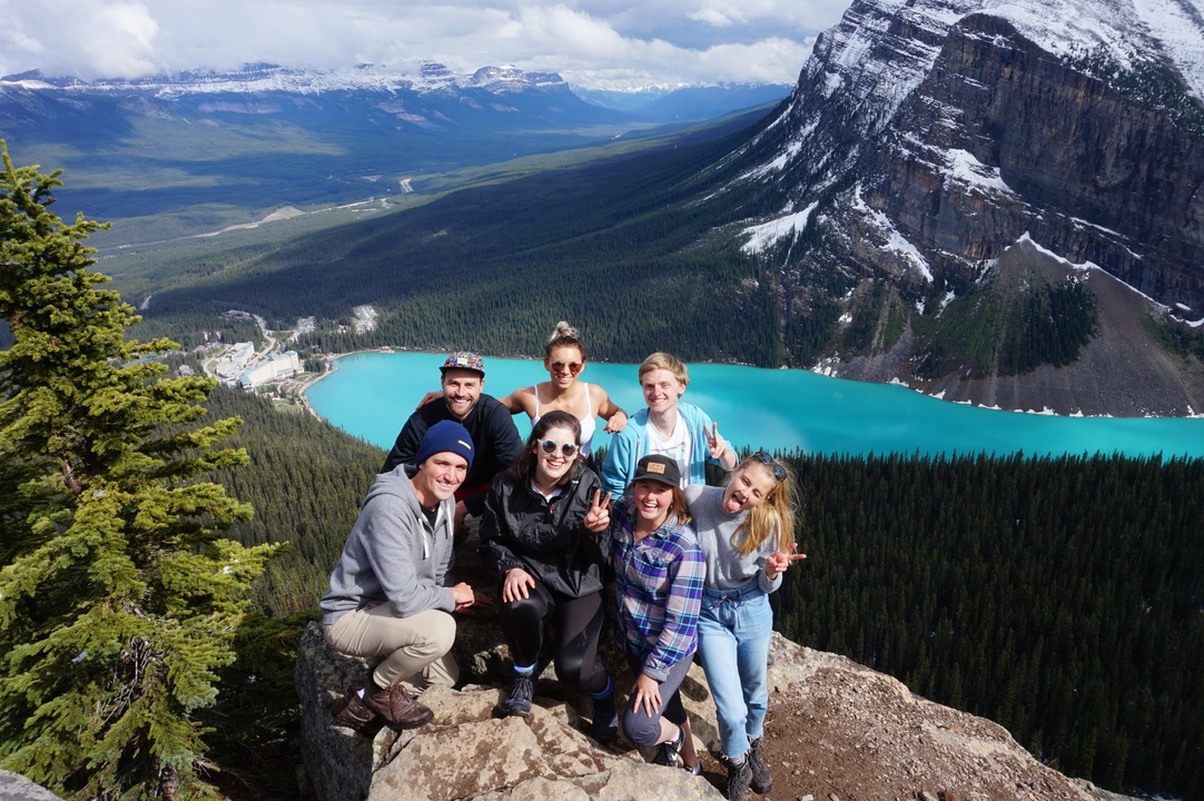 Gruppe von Wanderern auf einer Klippe mit Blick auf einen türkisfarbenen See.