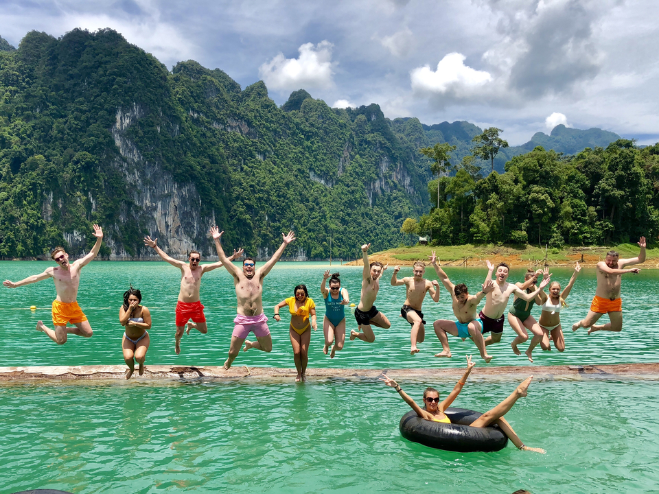 Group jumping with joy on a floating platform with mountains in the background.