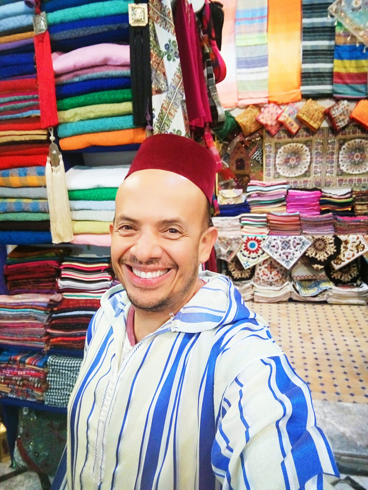 Person wearing traditional attire in a colorful market.