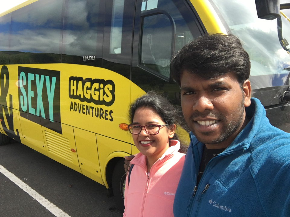 Two people posing in front of a Haggis Adventures tour bus.