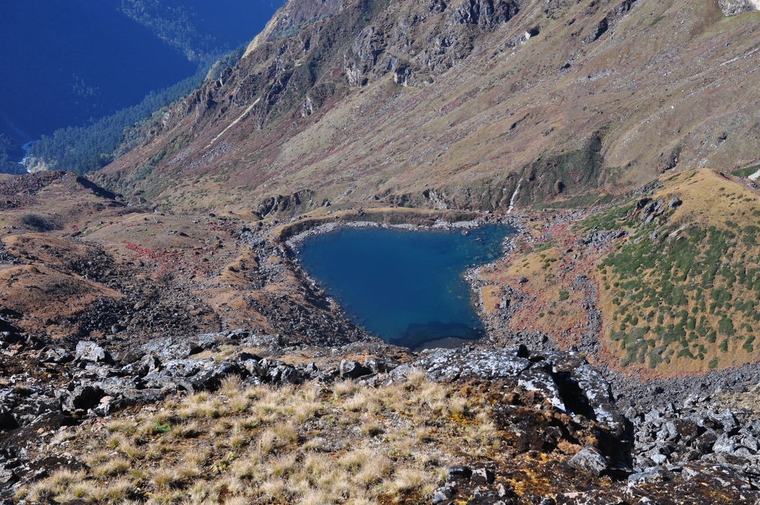 A heart-shaped turquoise alpine lake nestles among steep, rocky Himalayan ridges.