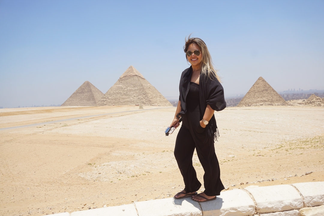 Person standing in front of the Pyramids of Giza with a bright sky.