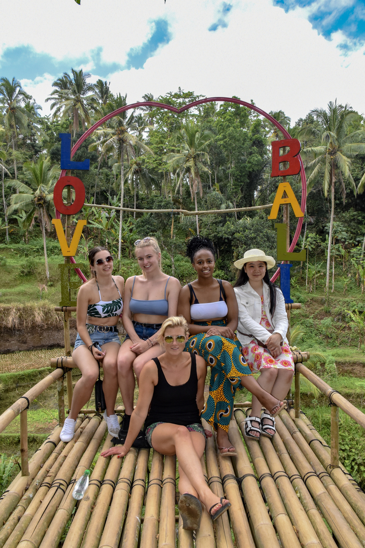 Five women sitting on a bamboo structure decorated with large colorful letters.
