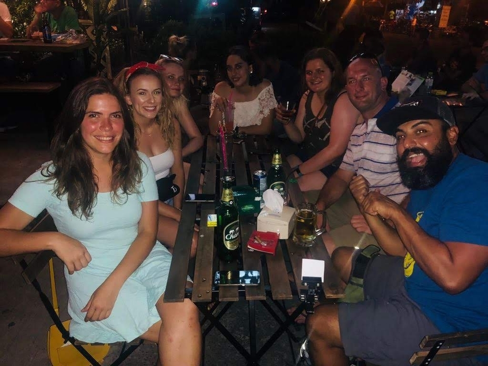 Groupe de personnes assises à une table avec des boissons dans un cadre faiblement éclairé.