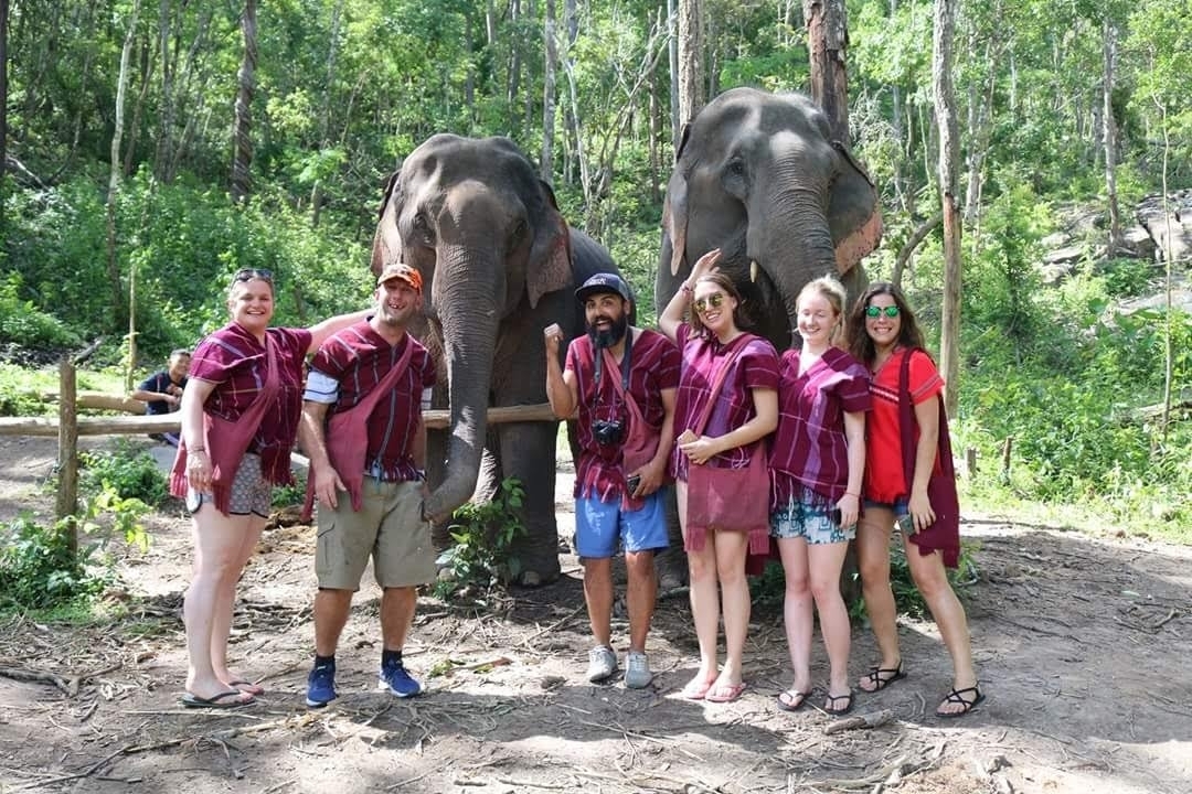 Groupe de personnes posant avec deux éléphants dans un cadre naturel.