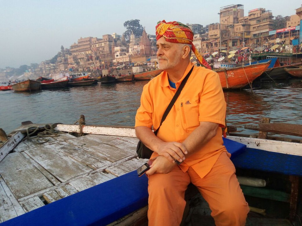 A man in traditional turban rides a wooden boat past the historic riverfront of Varanasi.