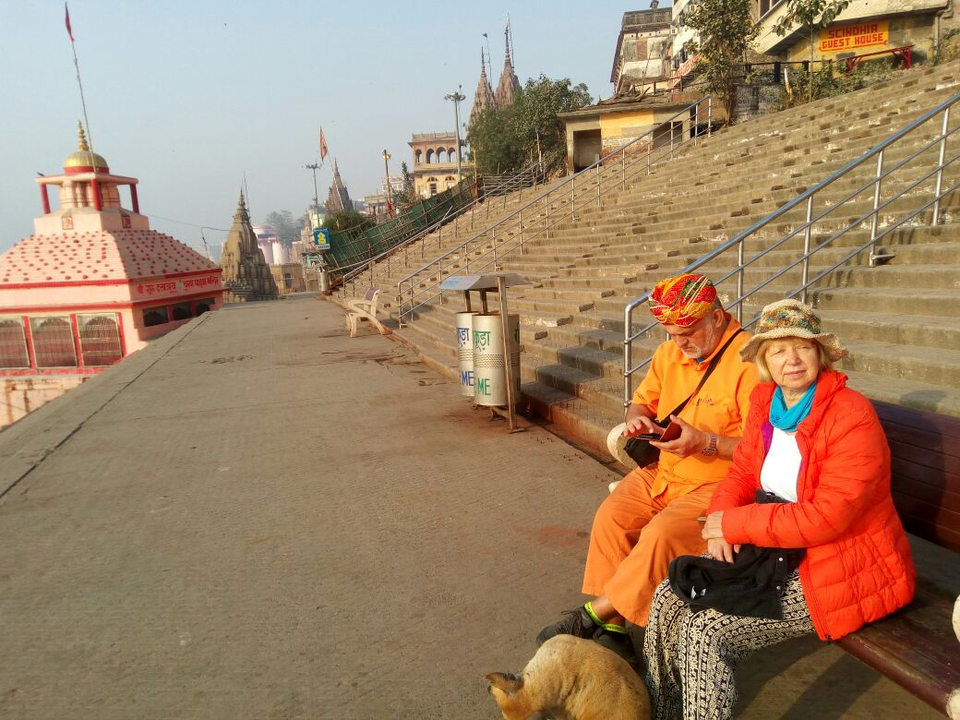 A senior couple dressed in bright colours rest on the wide steps of a river ghat in Varanasi.