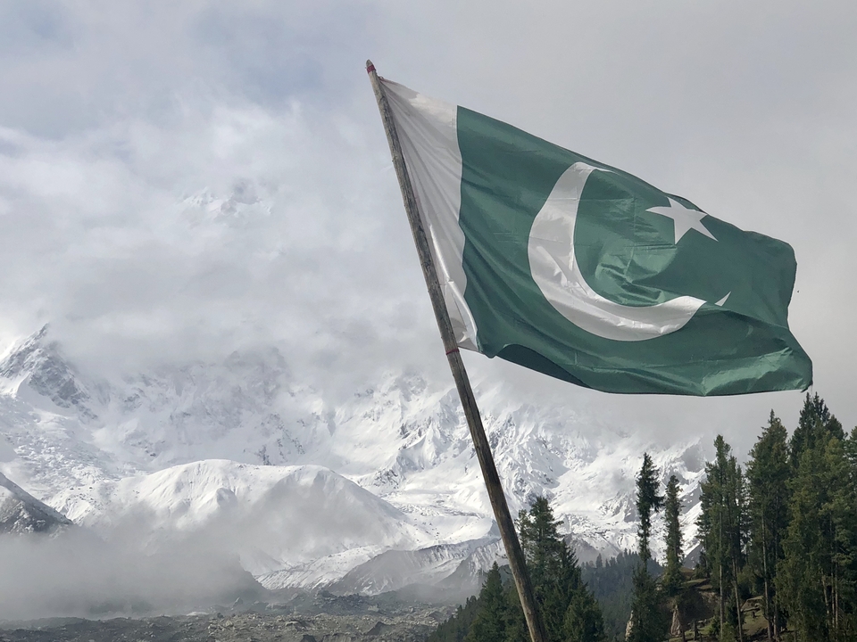 Flag of Pakistan with snowy mountains in the background.