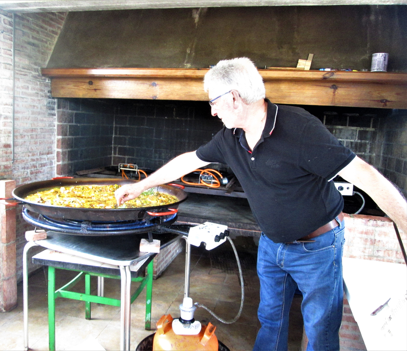 Homme cuisinant une grande paella en plein air.