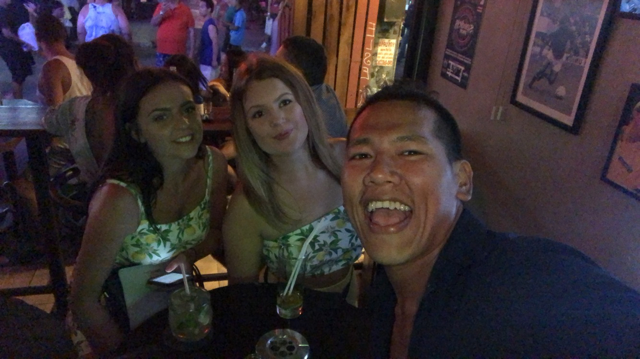 Three people posing with drinks at a crowded bar.