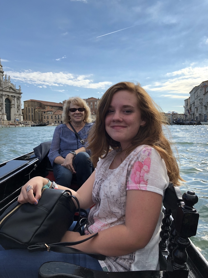 Deux personnes sur un bateau avec des bâtiments vénitiens en arrière-plan.