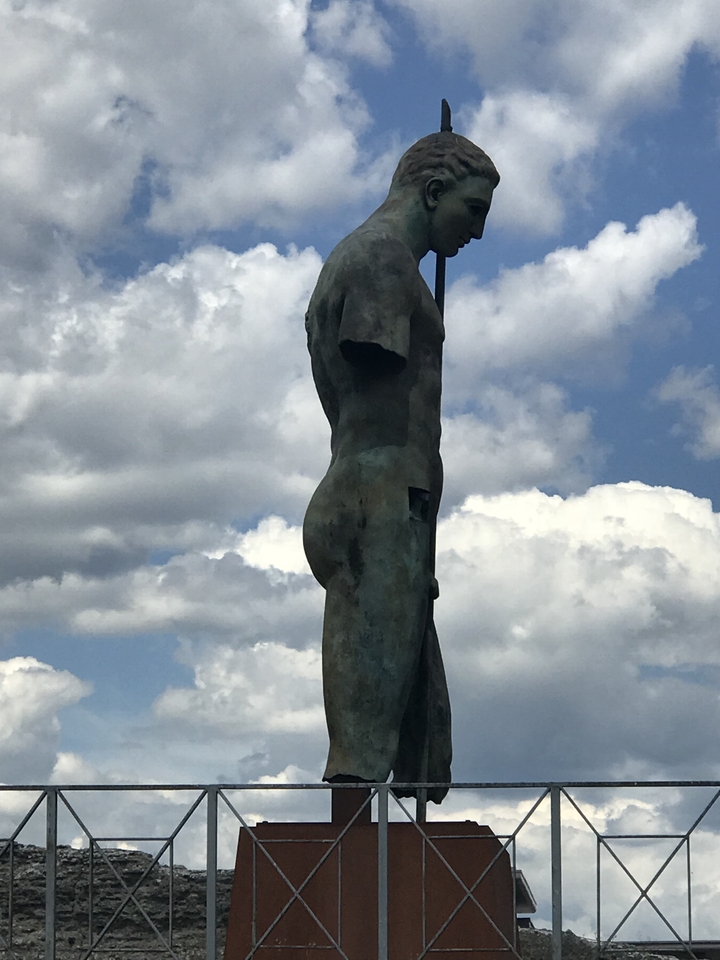 Statue d'un personnage debout sur fond de ciel nuageux.
