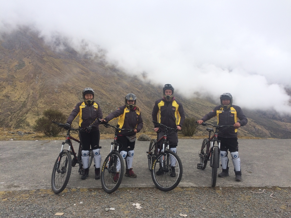 Groupe de cyclistes en tenue de protection sur un chemin de montagne sous un ciel nuageux.