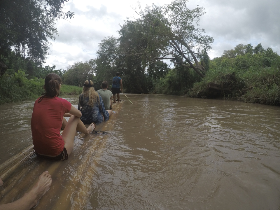 Group of people rafting down a river on a bamboo raft.